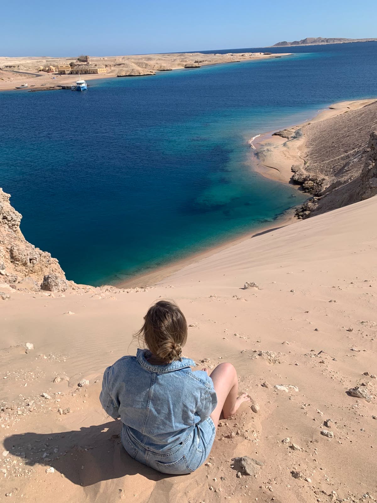 A guest sitting on a sand dune looking over a turquoise bay.