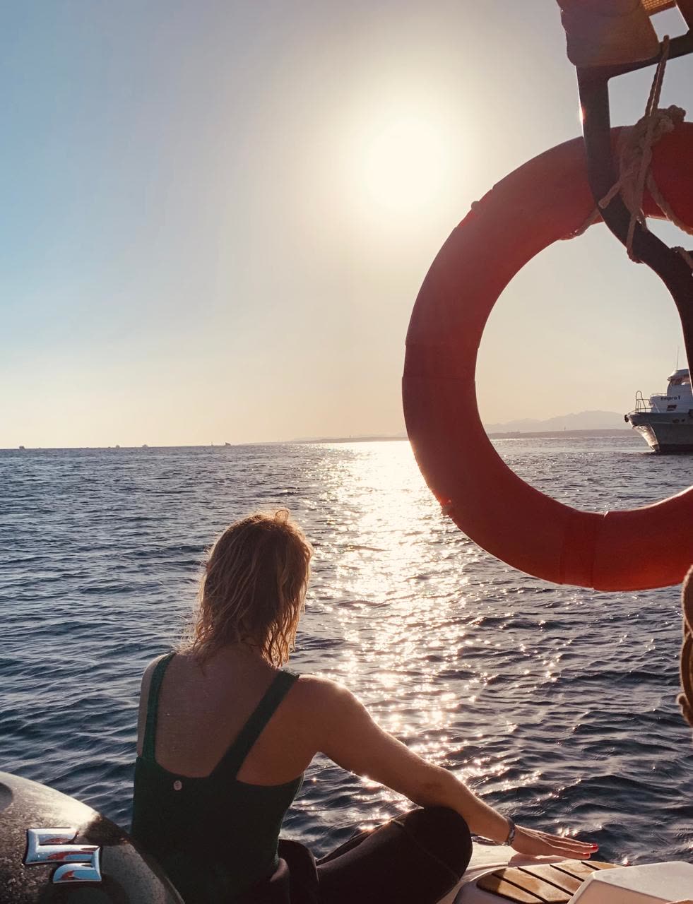 A guest sitting at the back of the boat by a life ring, sun on the water.